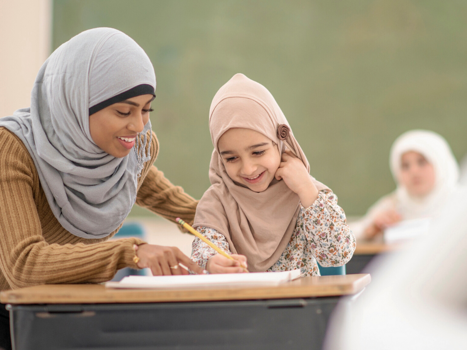 A teacher and a student writing together in a classroom.