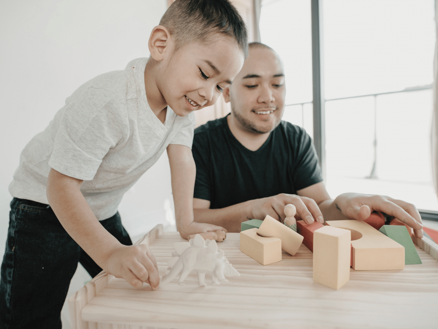 A child and a parent improving confidence using building blocks and toy dinosaurs.